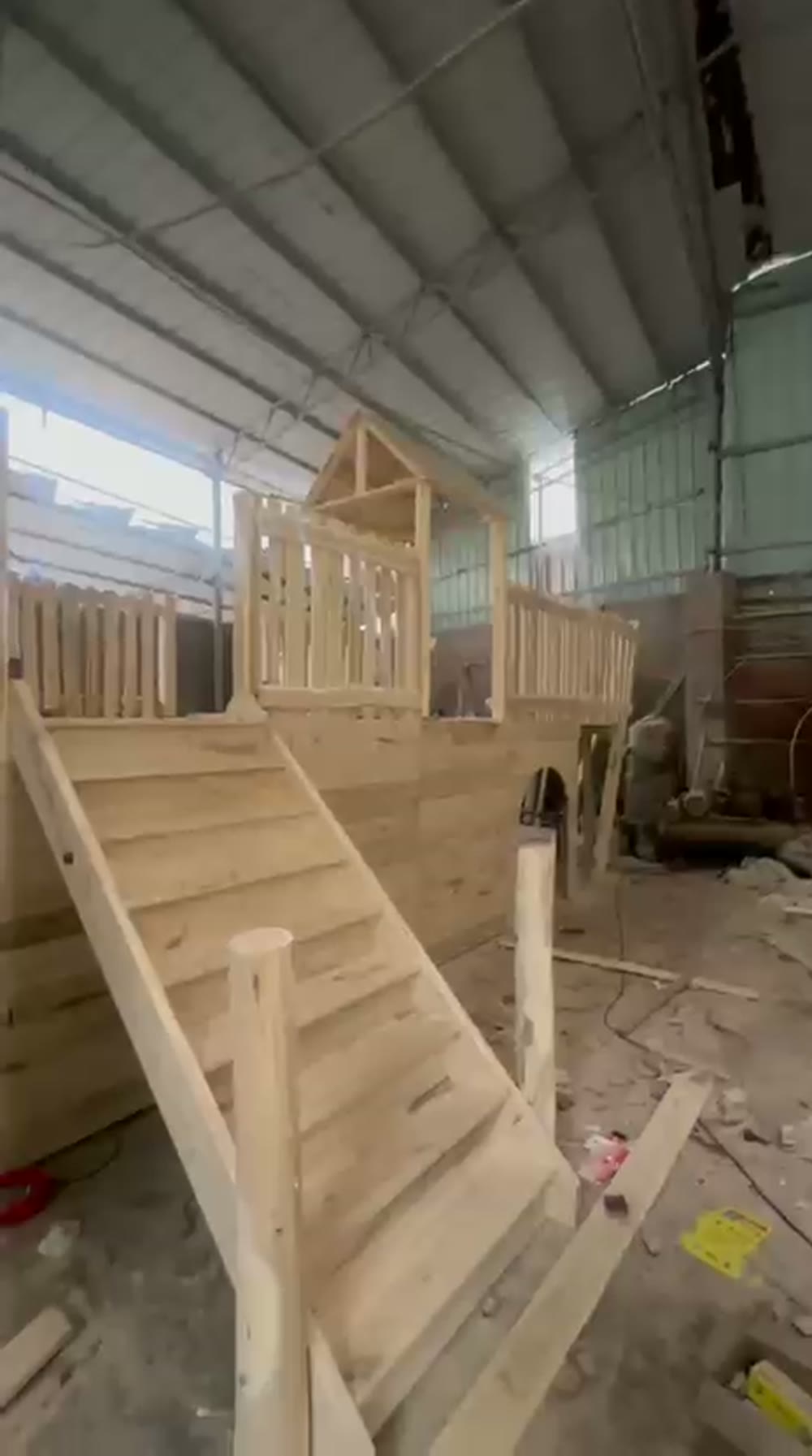 The wooden pirate ship playground hull under assembly in the workshop, showing the boarding stairs, railings and crow's nest watchtower taking shape.